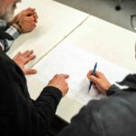 Konstruktionspläne auf einem Tisch, um den drei Männer stehen und beraten